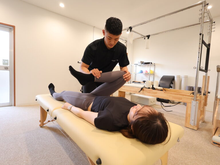 ストレッチベッドで、トレーナーに脚を伸ばしてもらう女性